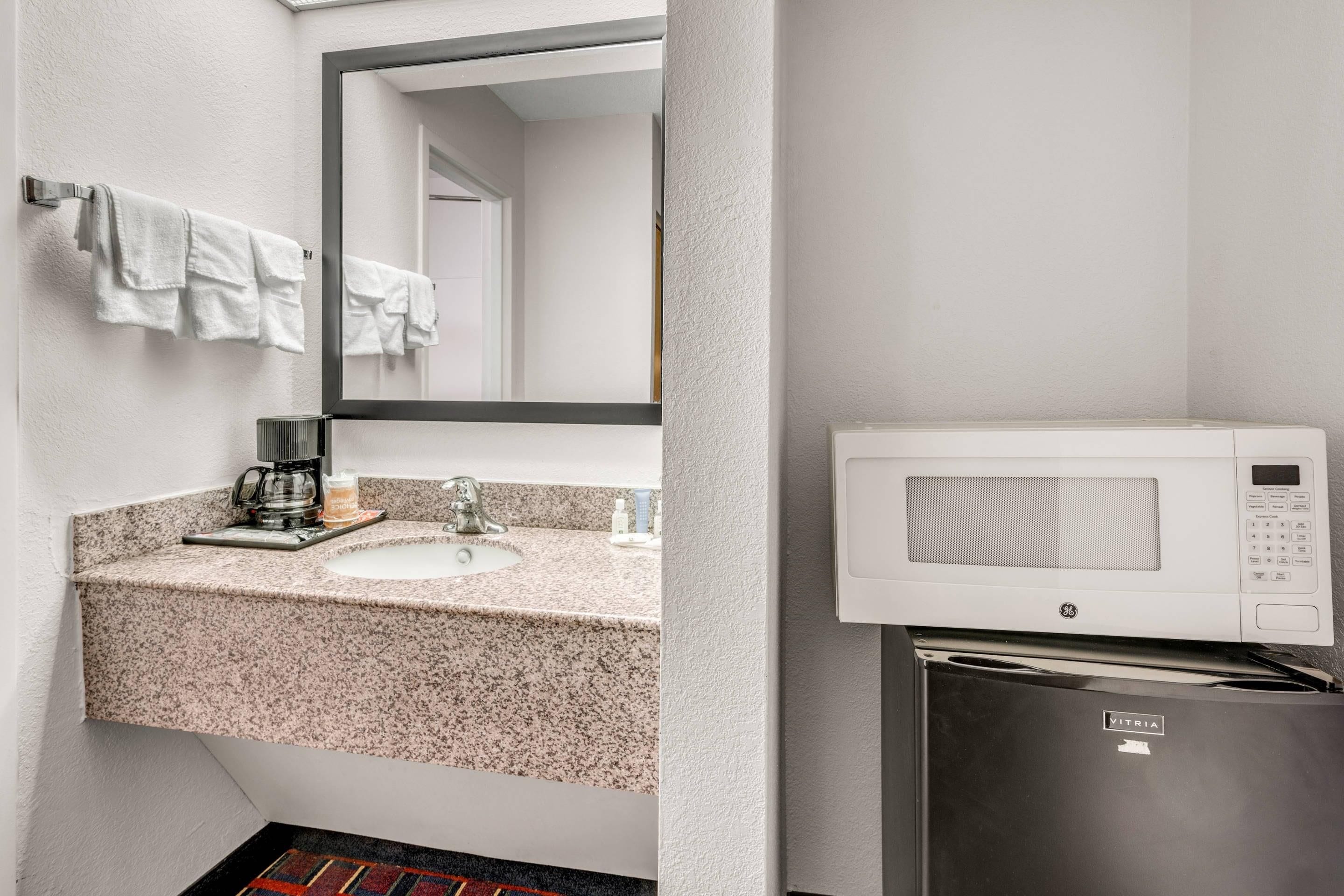 Ein modernes Badezimmer mit Granitplatte, Kaffeemaschine, Waschbecken und Mikrowelle.
