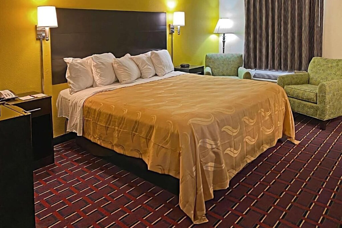 A hotel room with a bed, two bedside lamps, a chair, a nightstand, and a curtain.