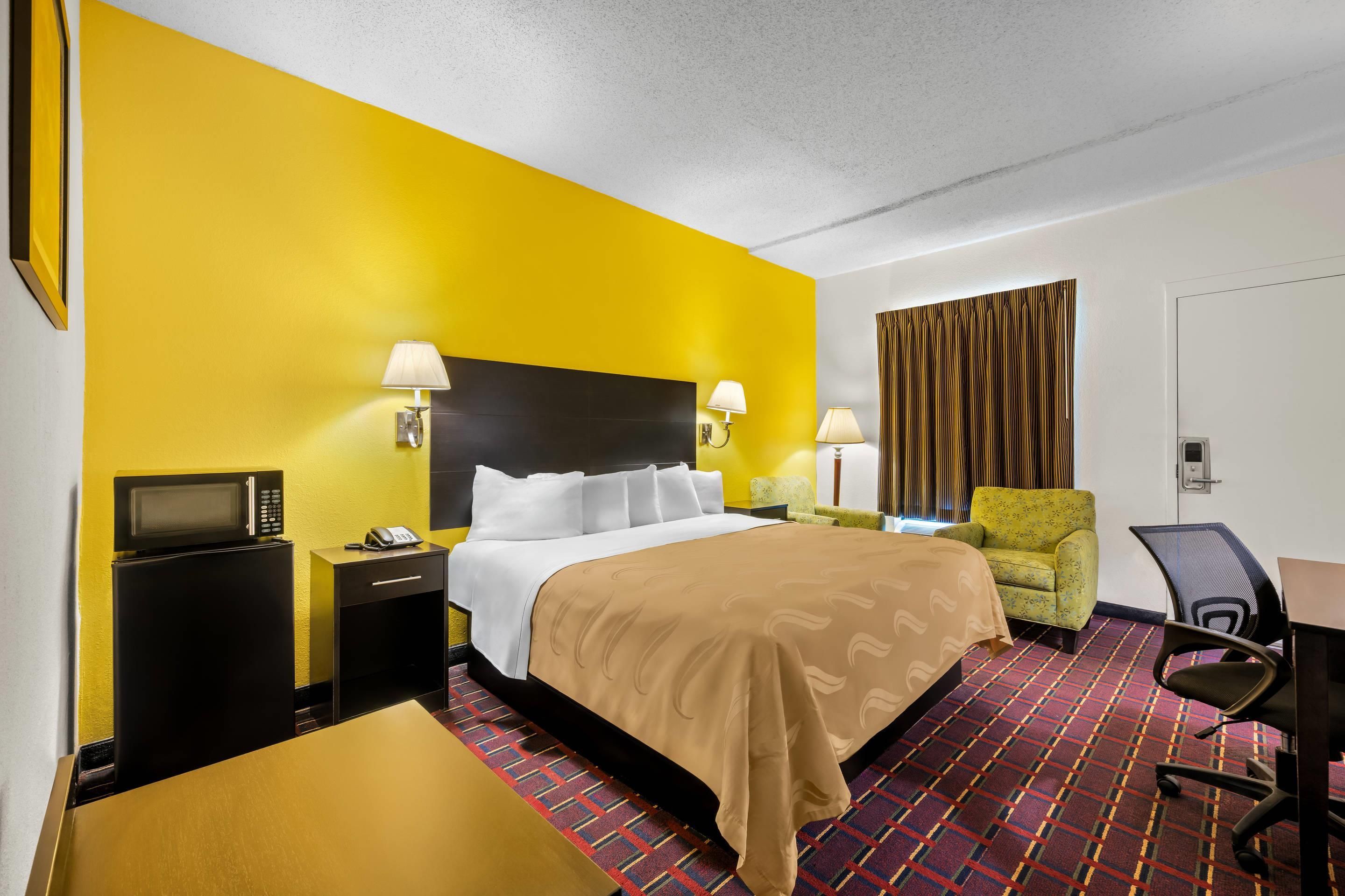 A hotel room with a bed, bedside tables, a desk, a chair, and a television.
