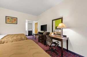 Una habitación de hotel con cama, escritorio, silla, televisión y un cuadro en la pared.