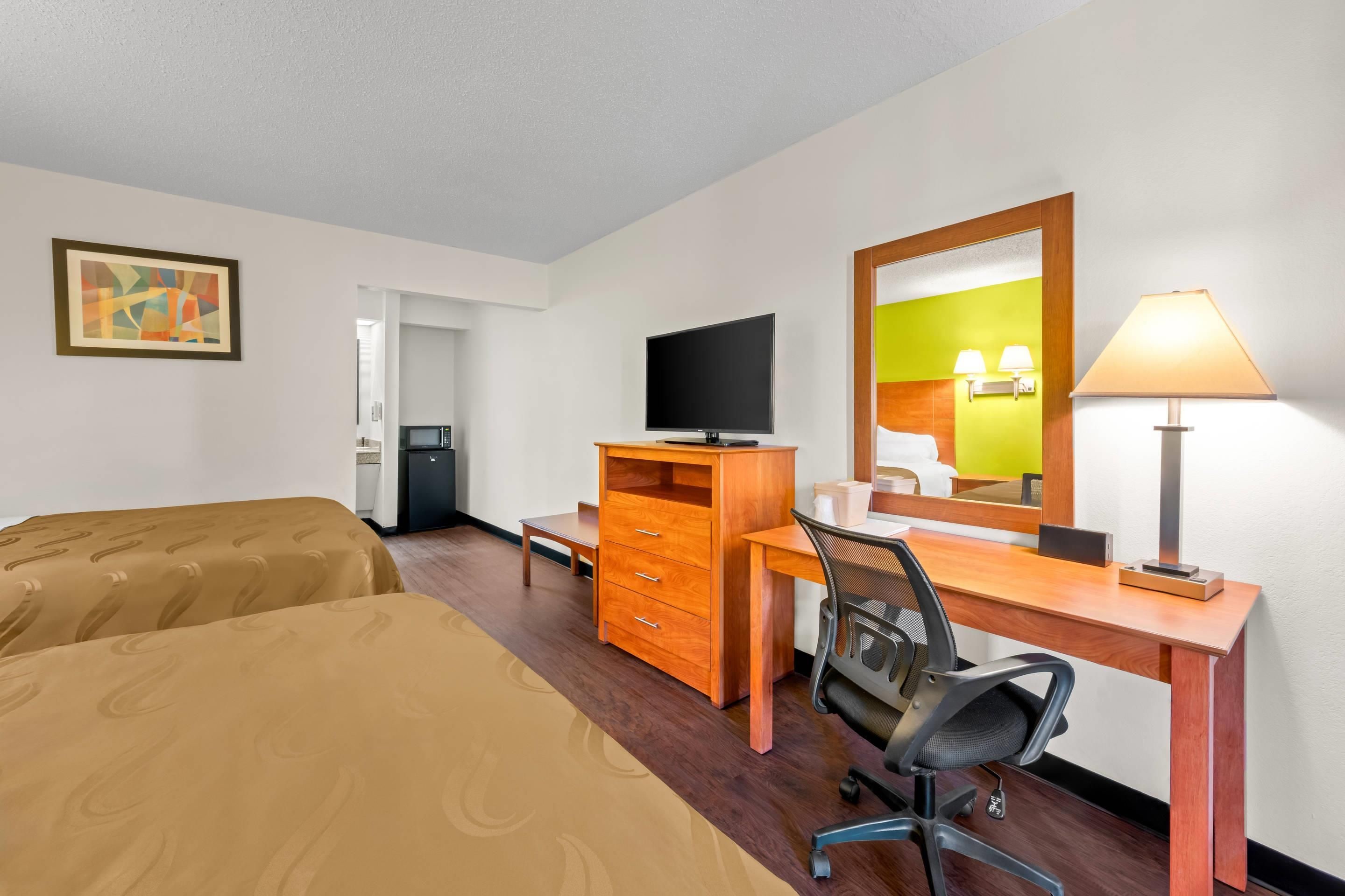 A hotel room with two beds, a desk with a chair, a television, a dresser, and a mirror.
