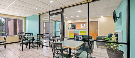 A modern hotel lobby with a glass partition, tiled flooring, and a variety of seating options including tables and chairs.