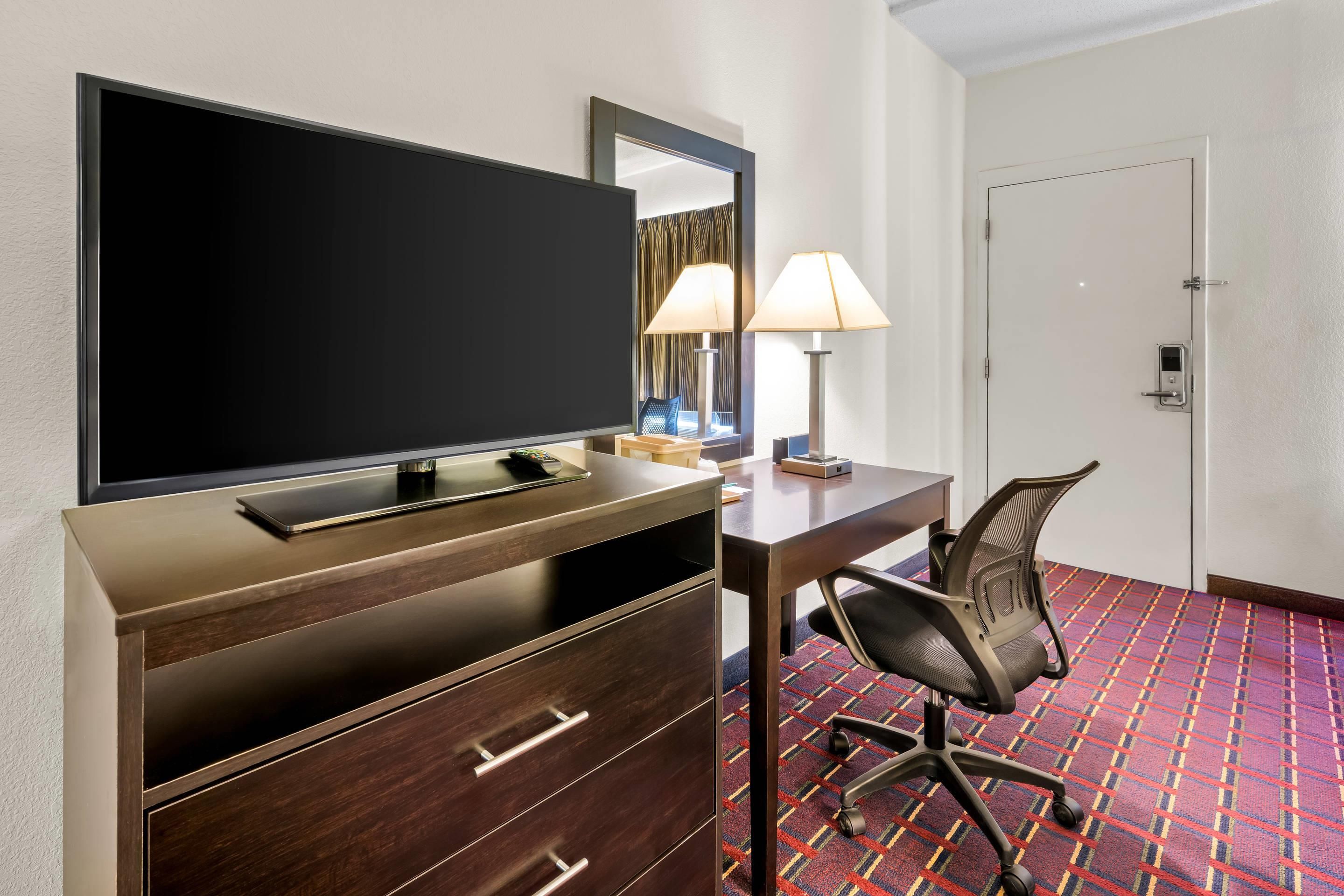 Una habitación de hotel con televisión, escritorio, silla, lámpara y puerta.