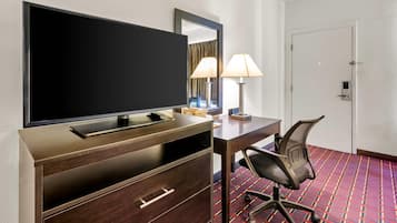 Una habitación de hotel con televisión, escritorio, silla, lámpara y puerta.