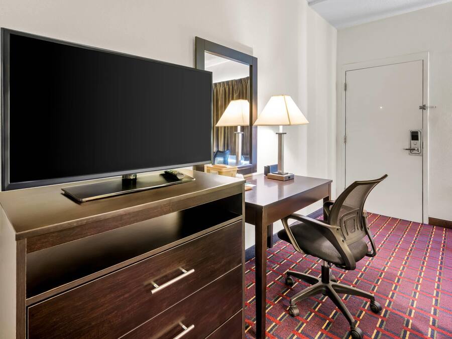 A hotel room with a TV, desk, chair, lamp, and a door.