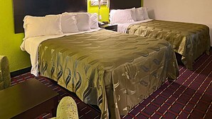 A hotel room with two beds, a nightstand, a lamp, and a check-in counter. - Quality Inn Henderson I-85 (Henderson)