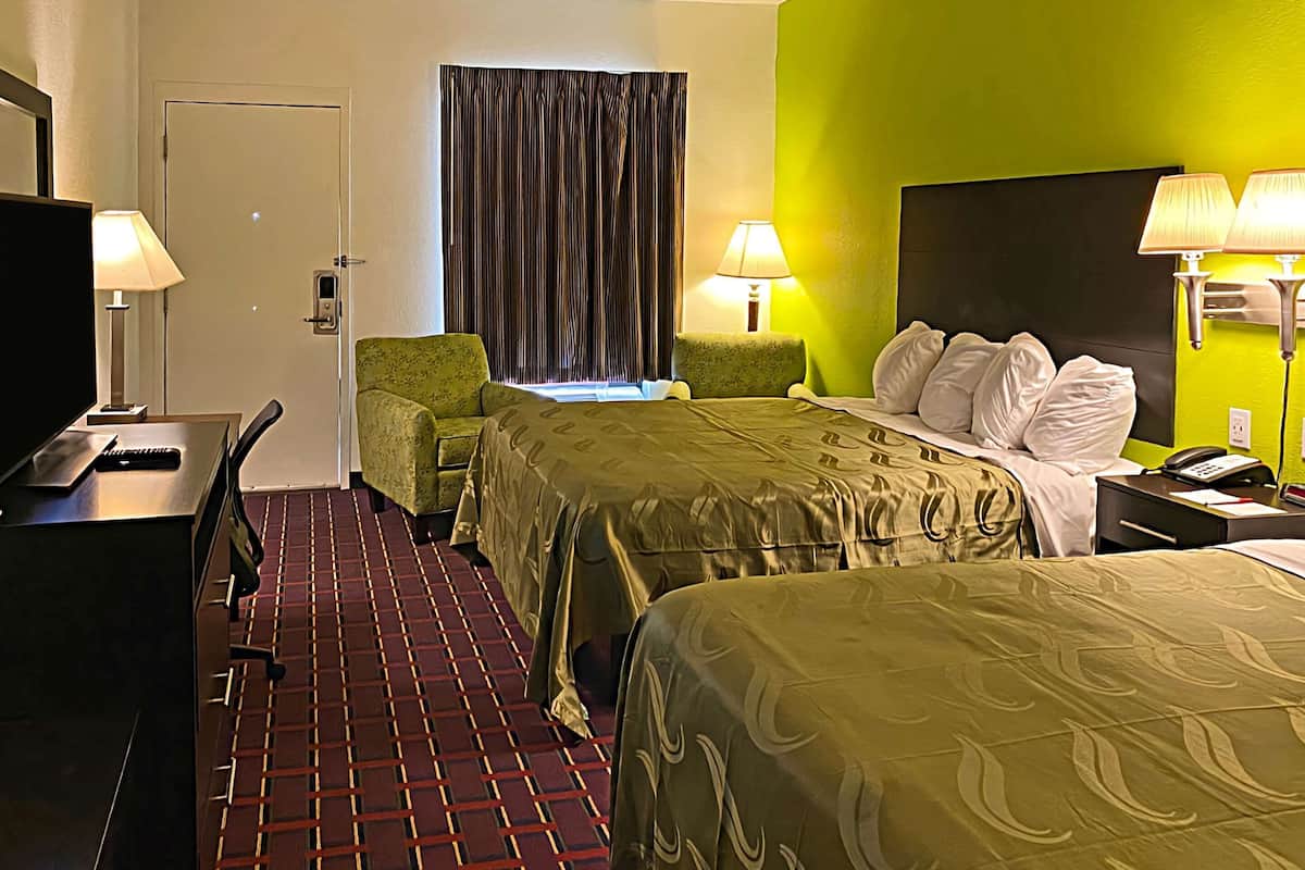 Ein Hotelzimmer mit zwei Betten, einem Schreibtisch, einem Stuhl, einem Fernseher und zwei Lampen.