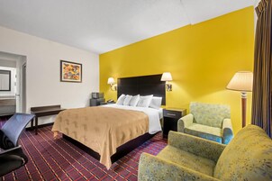 Habitación de hotel con cama, dos mesitas de noche, una silla, escritorio, lámpara, televisor y alfombra estampada.