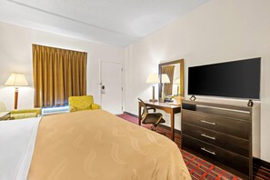 A hotel room with a bed, a desk, a chair, a television, and a wardrobe.