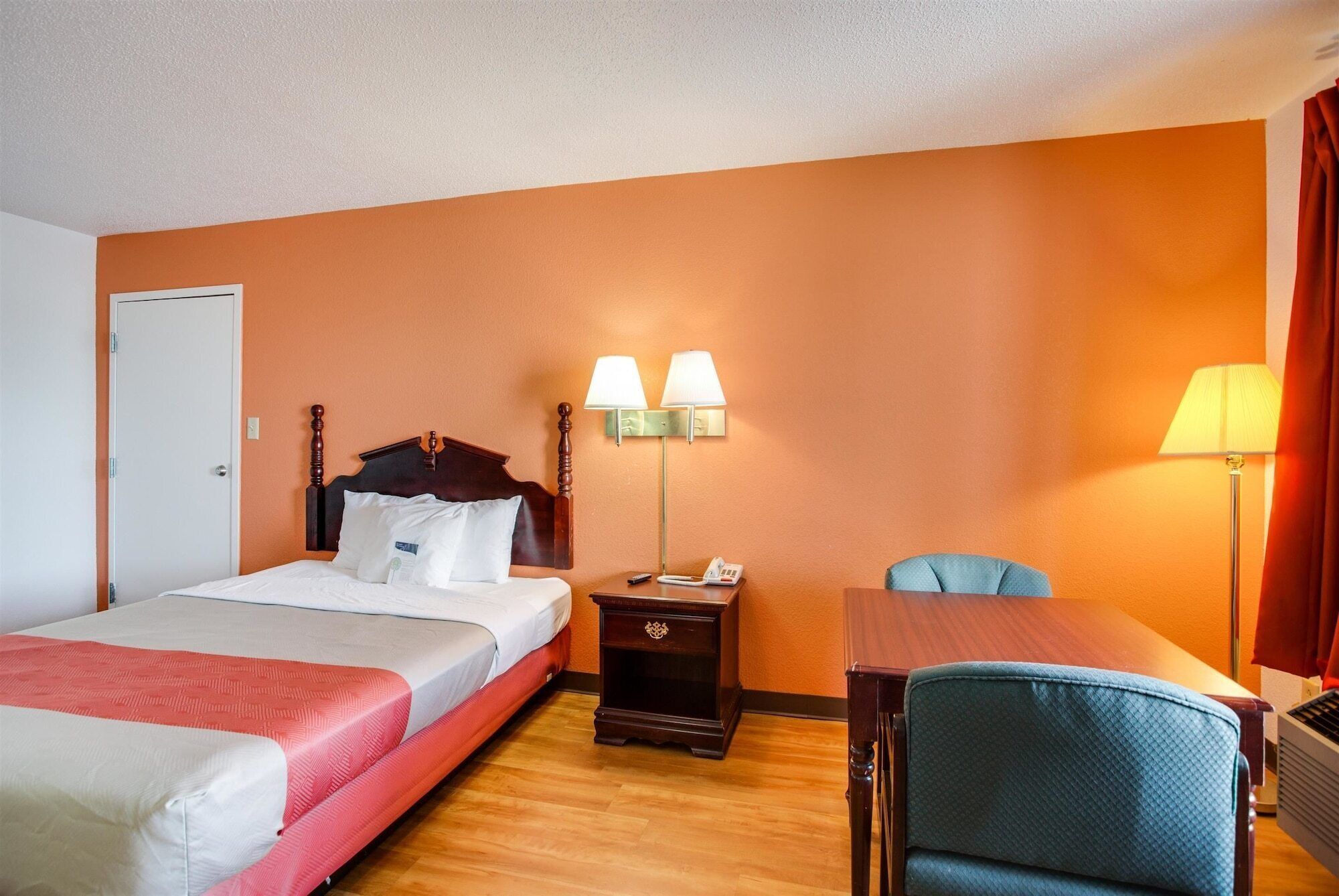 Una habitación de hotel con cama, mesita de noche, lámpara, silla y escritorio.
