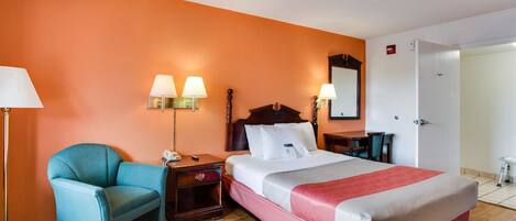 A hotel room with a bed, a chair, a nightstand, a lamp, and a mirror.