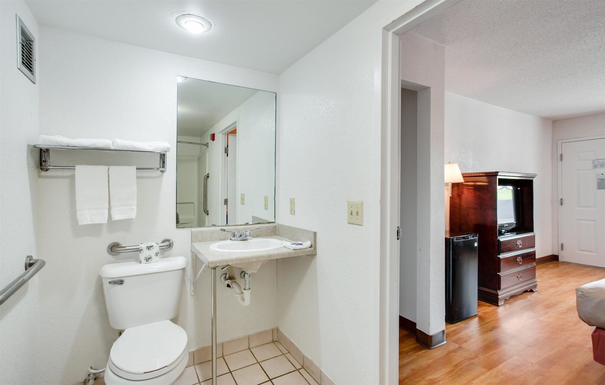 Un baño compacto con inodoro, lavamanos y espejo. Se observa un vestidor al fondo.