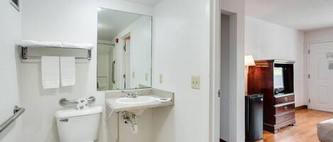 Un baño compacto con inodoro, lavamanos y espejo. Se observa un vestidor al fondo.