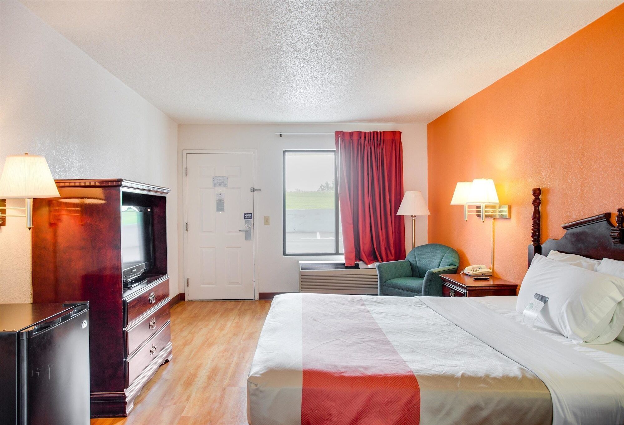 Habitación de hotel con cama, escritorio, silla, televisor y lámpara.