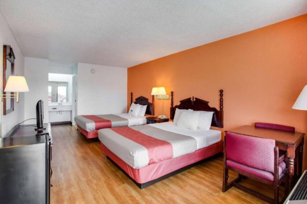 A hotel room with two beds, a desk, a chair, and a television.