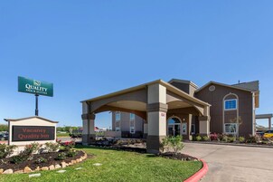 Un Quality Inn con entrada cubierta, un letrero que indica habitaciones disponibles y un jardín ajardinado.
