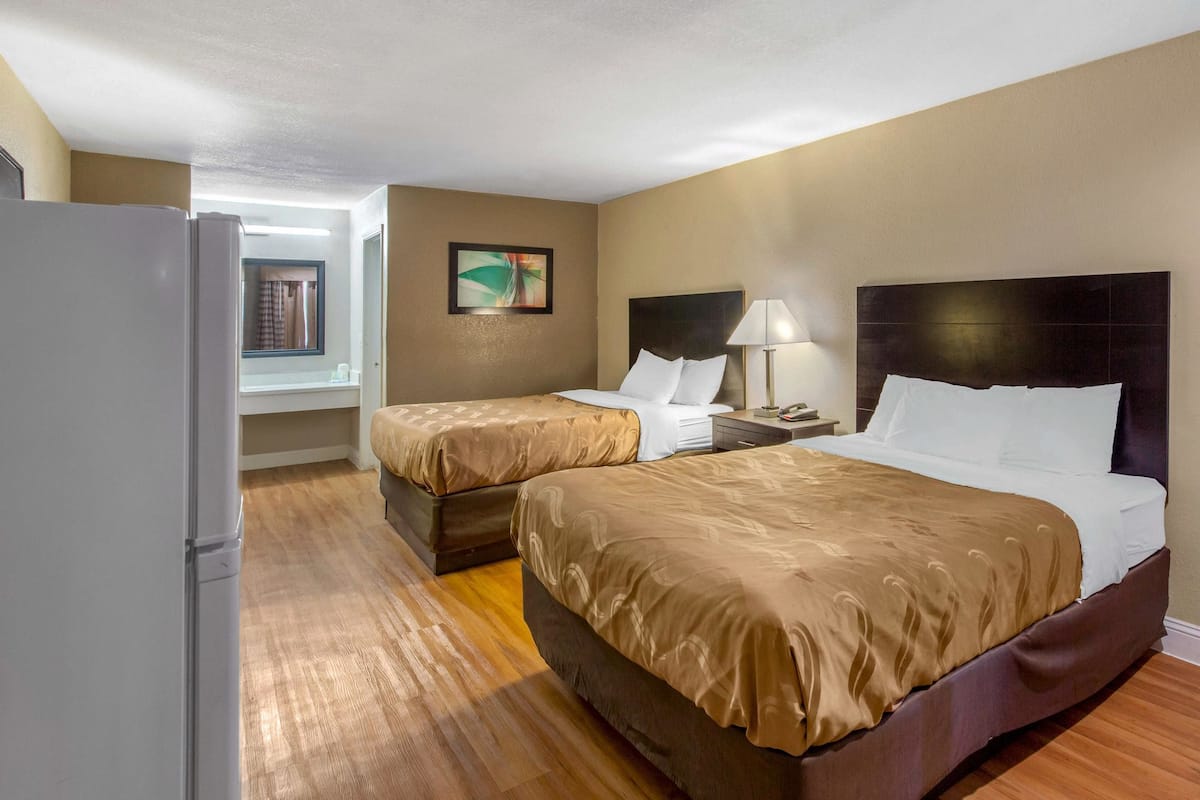 A hotel room with two beds, a refrigerator, a nightstand, and a window with curtains.