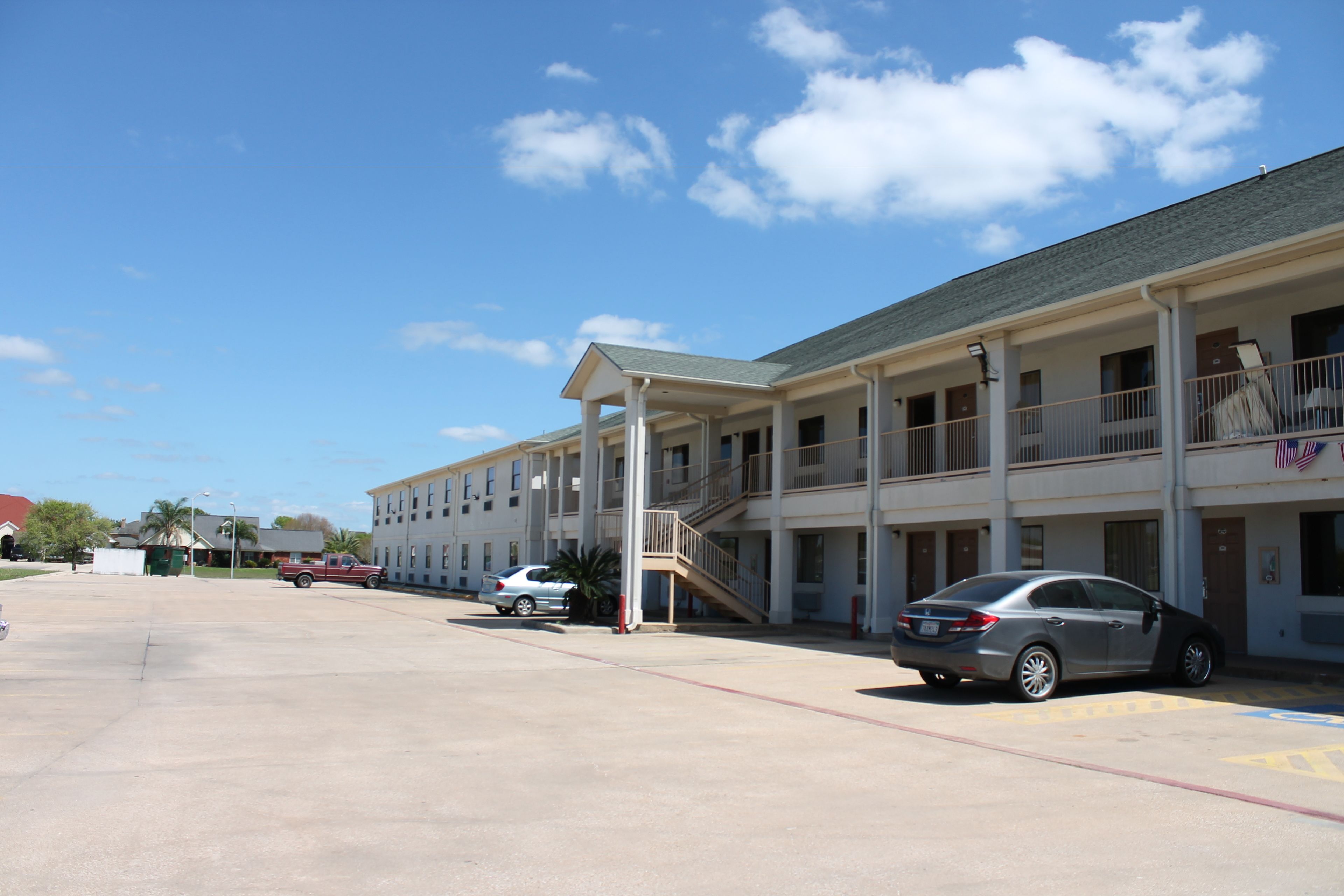 A motel with a covered parking area, multiple floors, and a staircase leading to the entrance.