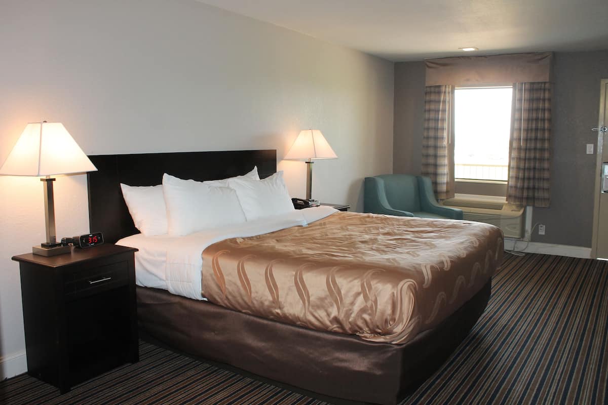 A hotel room with a large bed, two bedside tables with lamps, a chair, and a window with curtains.