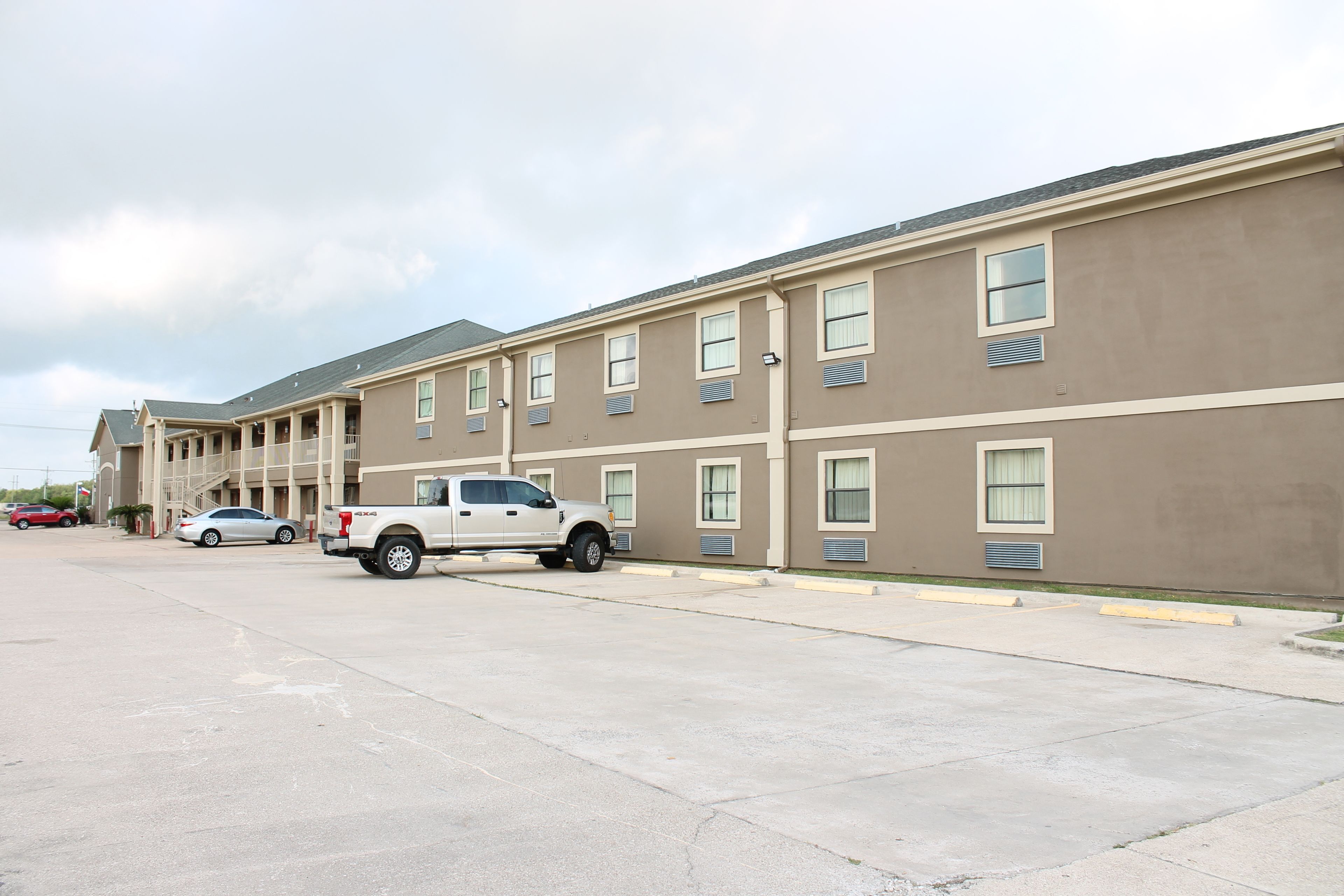 A multi-story hotel with a row of rooms, a parking lot, and a white pickup truck parked in front.