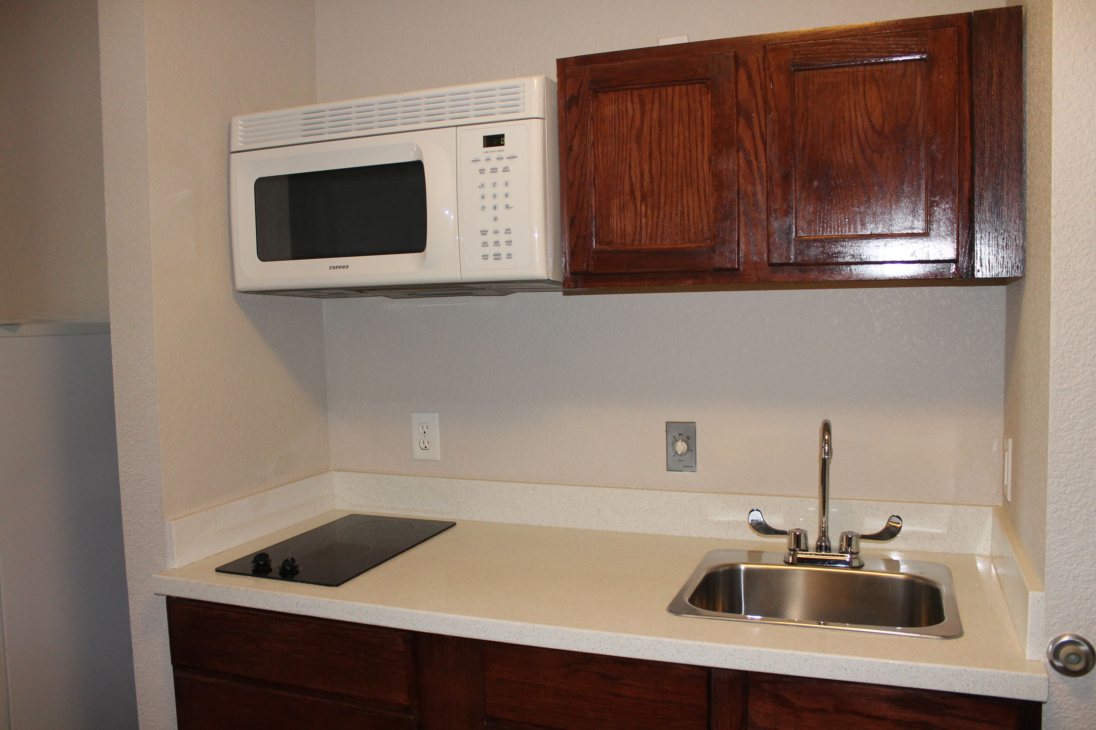 A compact kitchen with a built-in microwave, a stainless steel sink, and wooden cabinets.