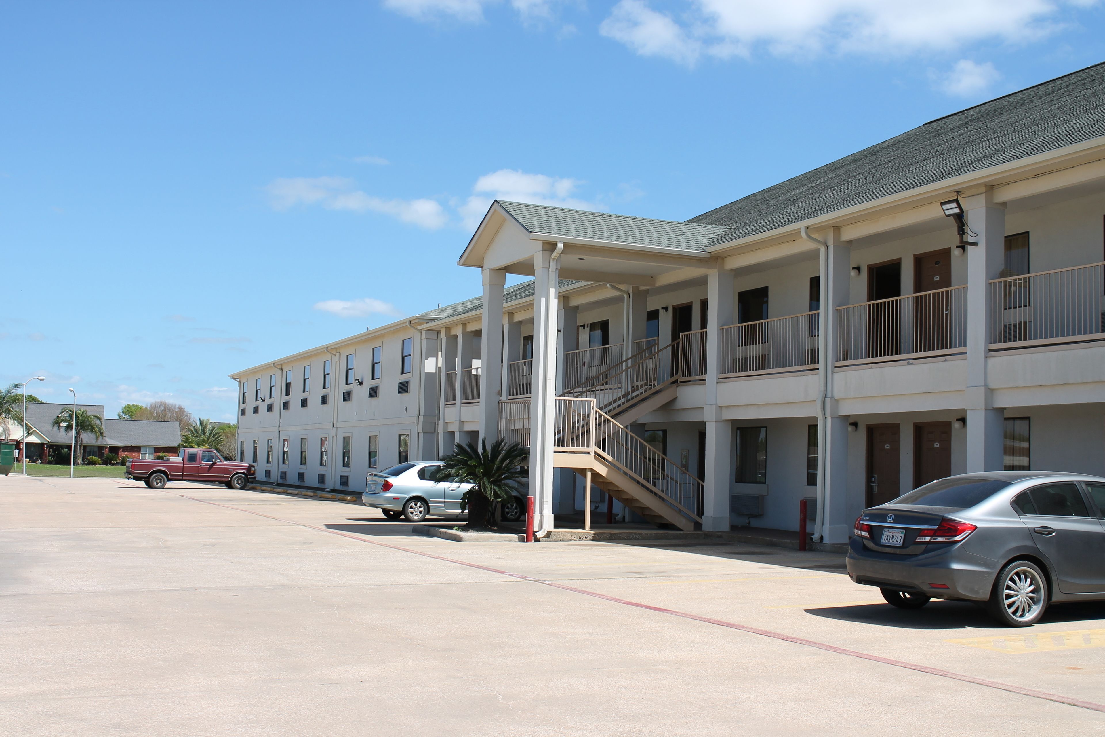 A multi-story motel with a covered parking area, a staircase leading to the upper floors, and a row of rooms with balconies.