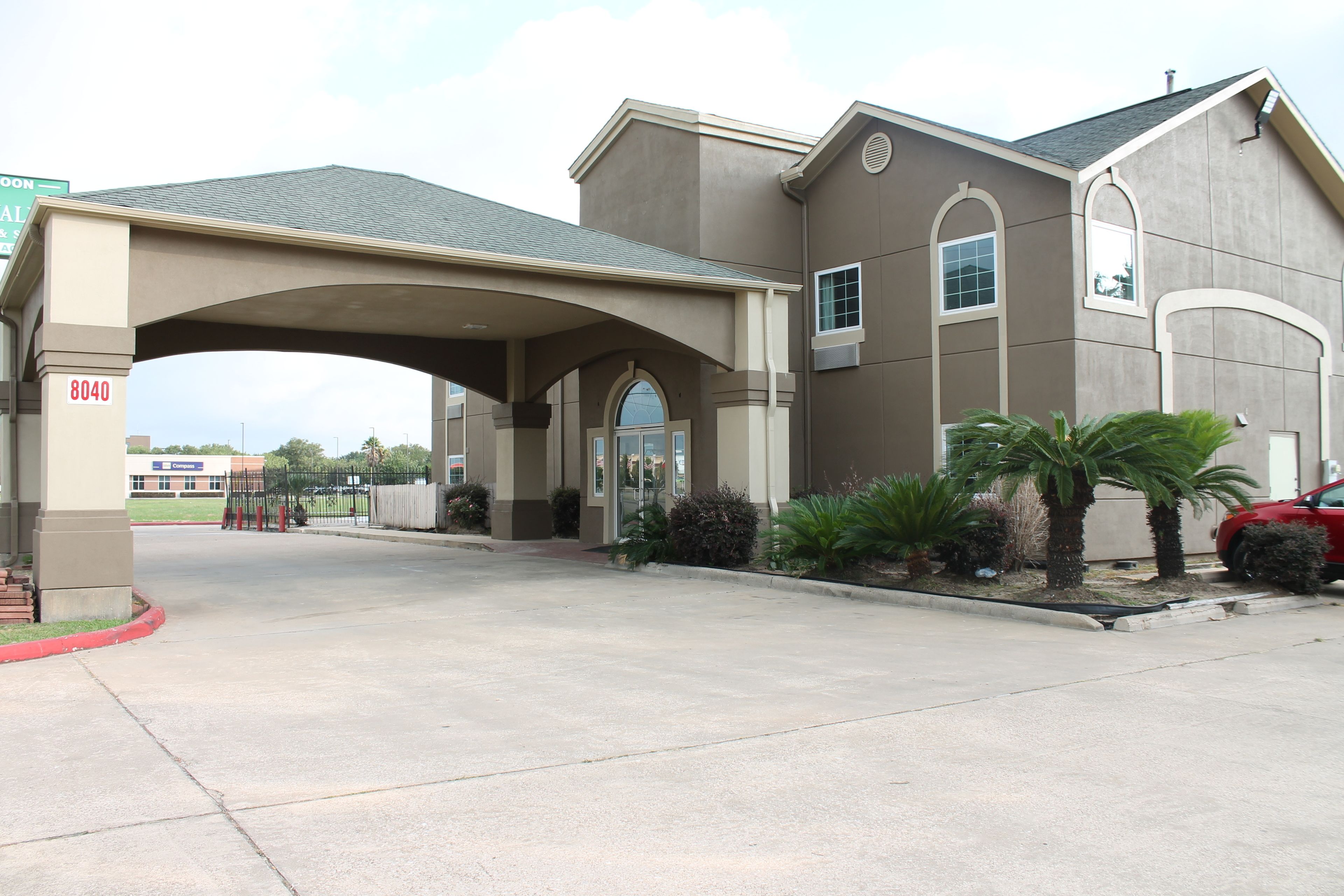 A building with a covered entrance, a parking area, and a red car parked nearby.