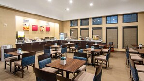 A spacious dining area with multiple tables and chairs, a counter with food and beverage options, and large windows providing natural light. - Comfort Suites NW Dallas Near Love Field (Dallas)