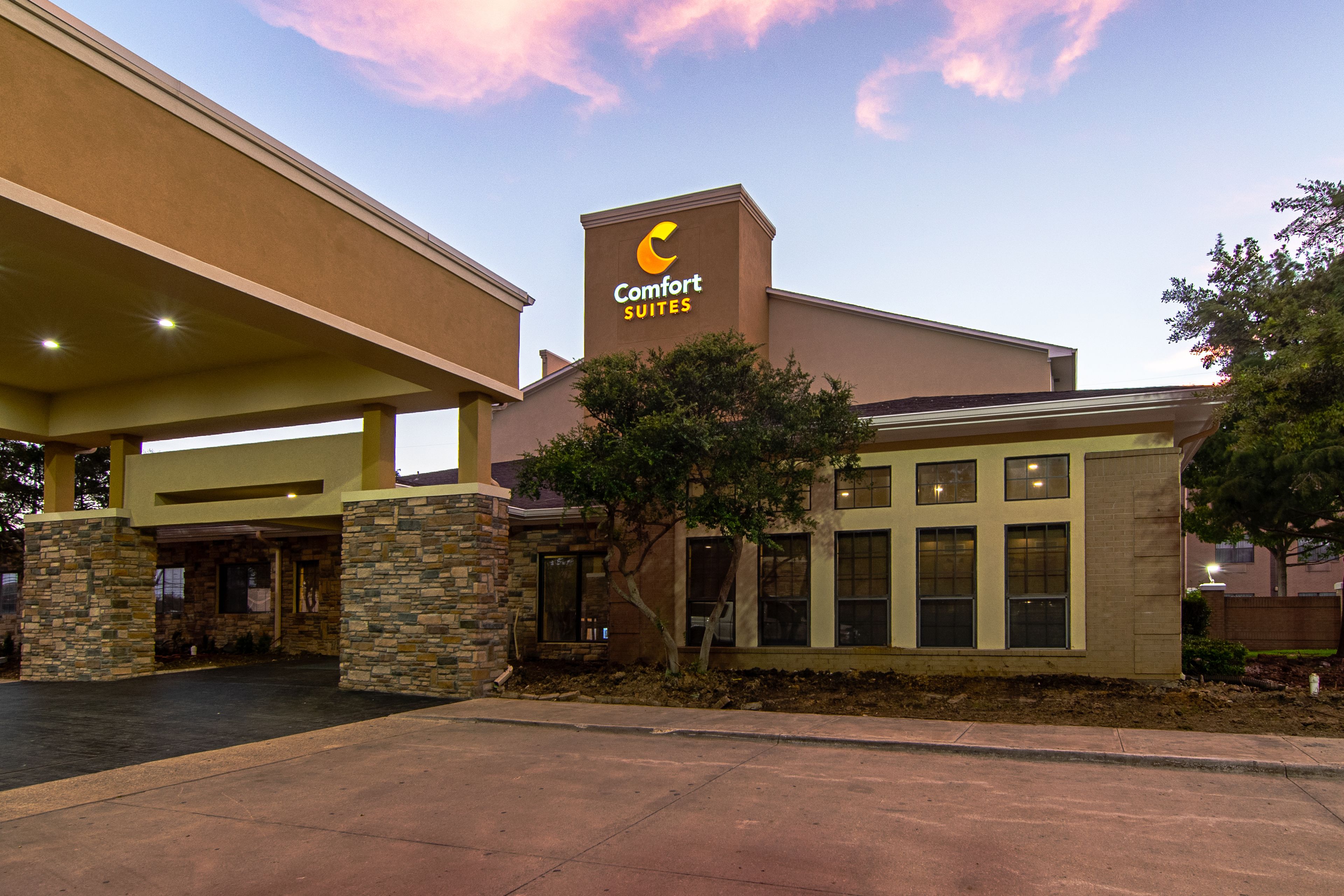 Ein Comfort Suites Hotel mit auffälliger Beschilderung, überdachtem Parkplatz und gepflegtem Vorgarten.