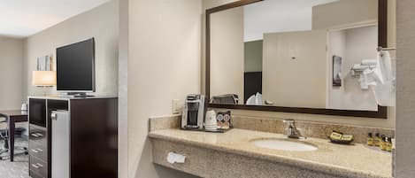 Un baño de hotel con lavamanos de encimera de granito, cafetera y espejo.