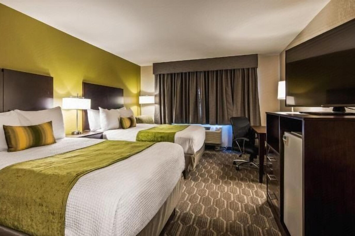 A hotel room with two beds, a desk, a television, and a window.