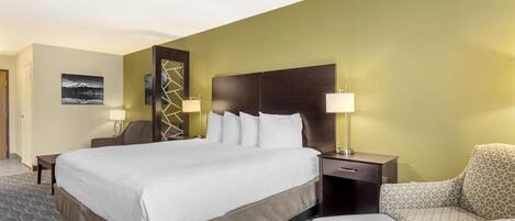 A hotel room with a large bed, two bedside tables with lamps, a patterned armchair, and a patterned sofa.