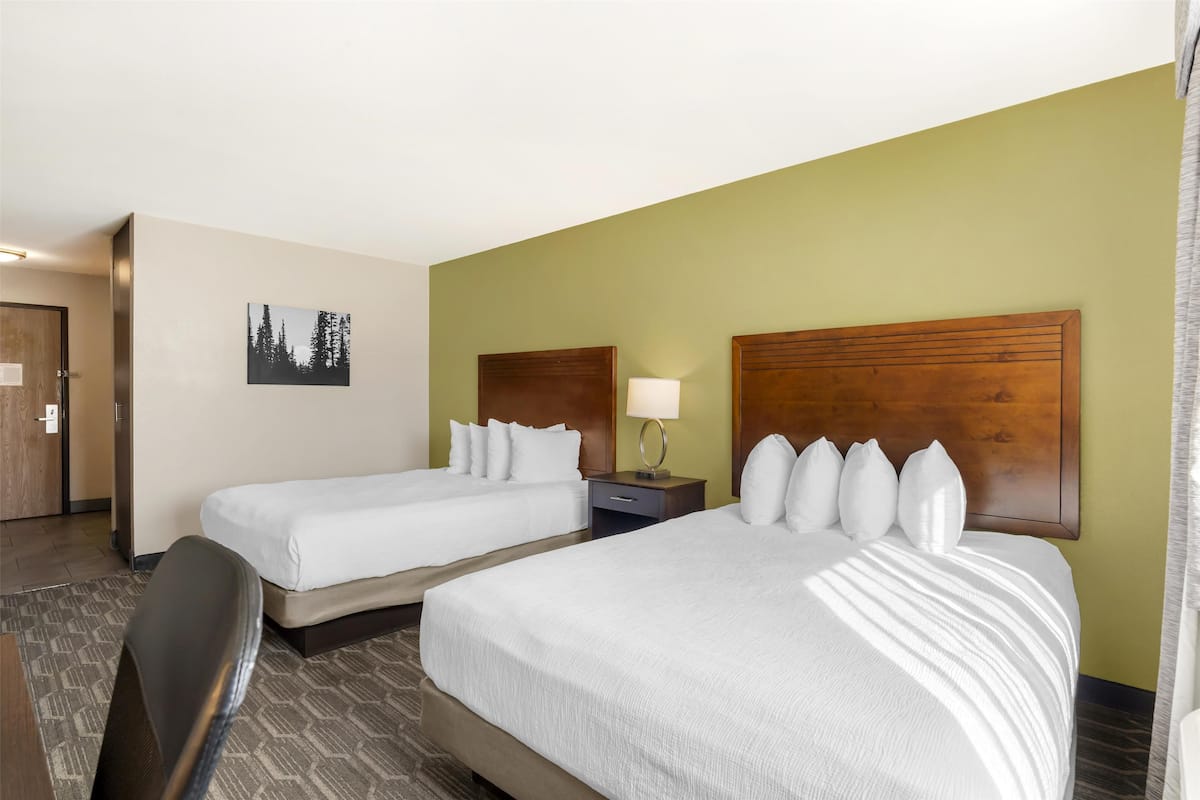 Une chambre d’hôtel avec deux lits, un bureau, une chaise, une table de chevet avec une lampe et un tableau encadré au mur.