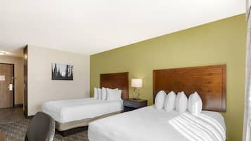 A hotel room with two beds, a desk, a chair, a nightstand with a lamp, and a framed picture on the wall.
