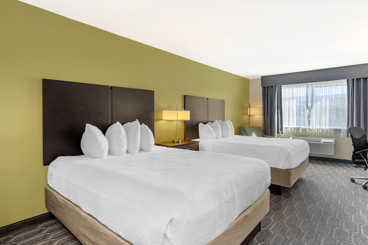 A hotel room with two beds, a desk, a chair, and a window with curtains.