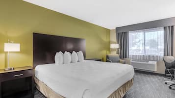 A hotel room with a large bed, a bedside table with a lamp, a chair, and a window with curtains.
