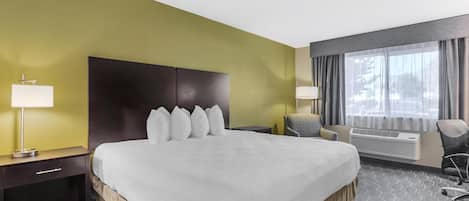 A hotel room with a large bed, a bedside table with a lamp, a chair, and a window with curtains.