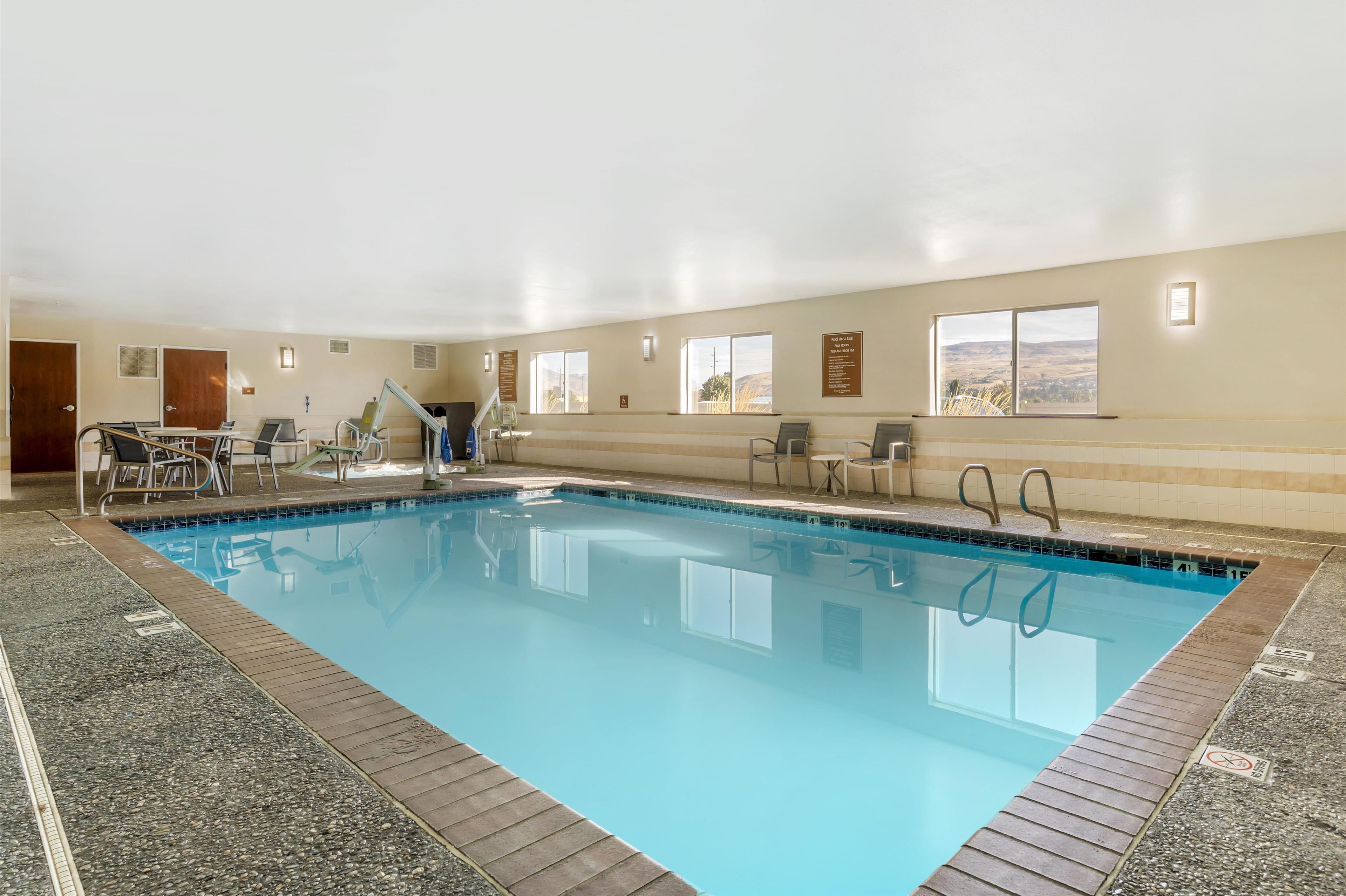 Piscina interna com água azul cristalina, rodeada por um deck revestido em azulejos e equipada com espreguiçadeiras e uma pequena mesa.