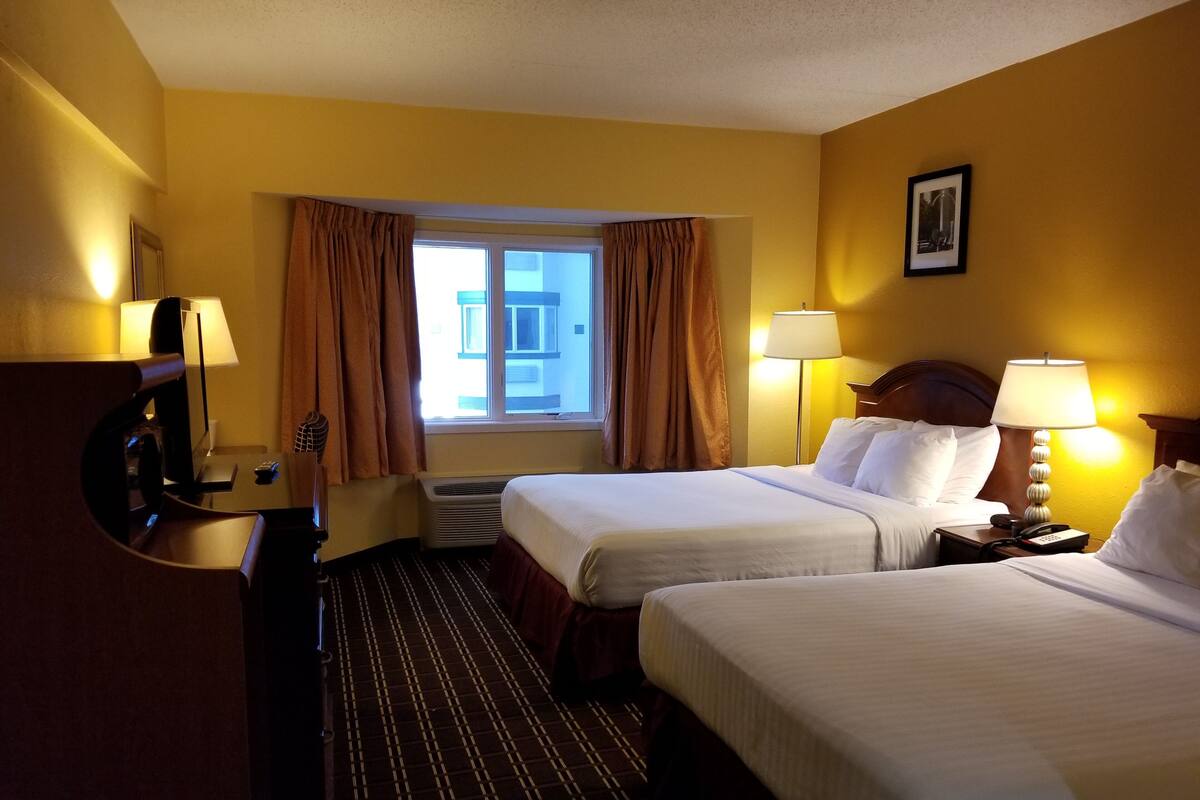 A hotel room with two beds, a desk with a lamp, a TV, and a window with curtains.