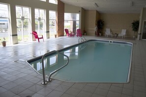 An indoor swimming pool with a tiled floor, a pool ladder, and several chairs around the pool area. - The Comstock Inn and Conference Center (Owosso)