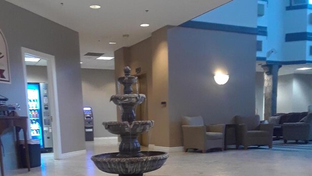 A lobby with a central fountain, seating area, and a vending machine. - The Comstock Inn and Conference Center (Owosso)