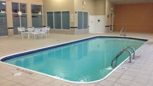 An indoor swimming pool with a tiled floor, a diving board, and a seating area with chairs. - The Comstock Inn and Conference Center (Owosso)