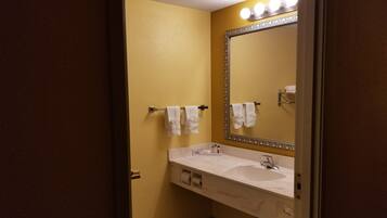 A bathroom with a white sink, a large mirror, and two towels hanging on towel bars.