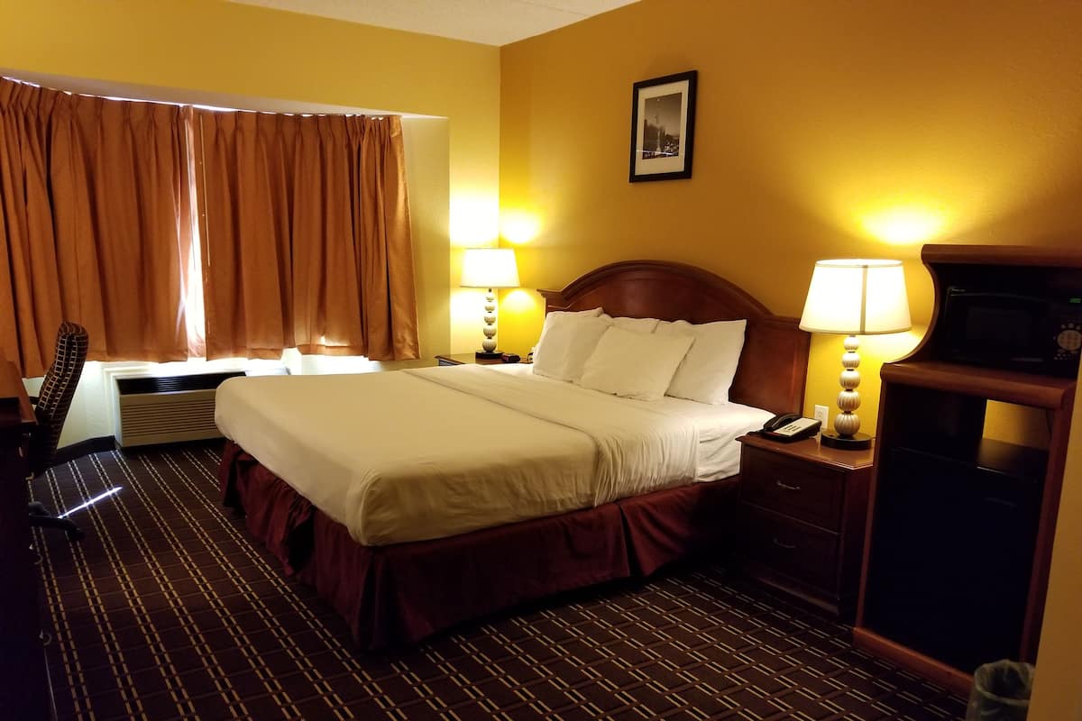 A hotel room with a large bed, two bedside lamps, a desk with a telephone, a chair, and a picture on the wall.