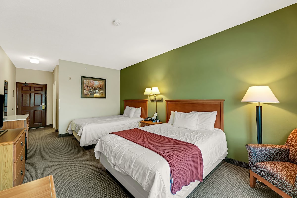 A hotel room with two beds, a desk, a chair, and a TV.