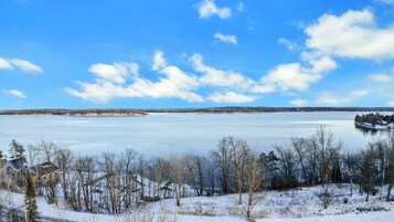 Un lago helado bajo un cielo despejado, rodeado de árboles cubiertos de nieve y una orilla distante.