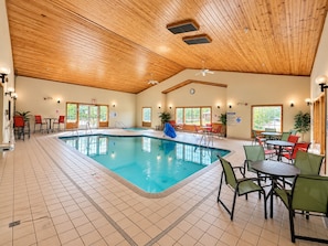 An indoor swimming pool with tiled flooring, wooden ceiling, and various seating arrangements.