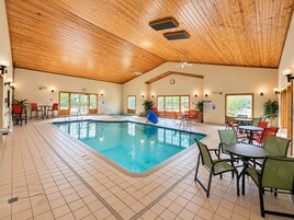Una piscina interior con suelo de baldosas, techo de madera y diferentes opciones de asiento.