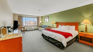 Habitación de hotel con cama, escritorio con lavamanos, silla, ventana con cortinas y lámpara.