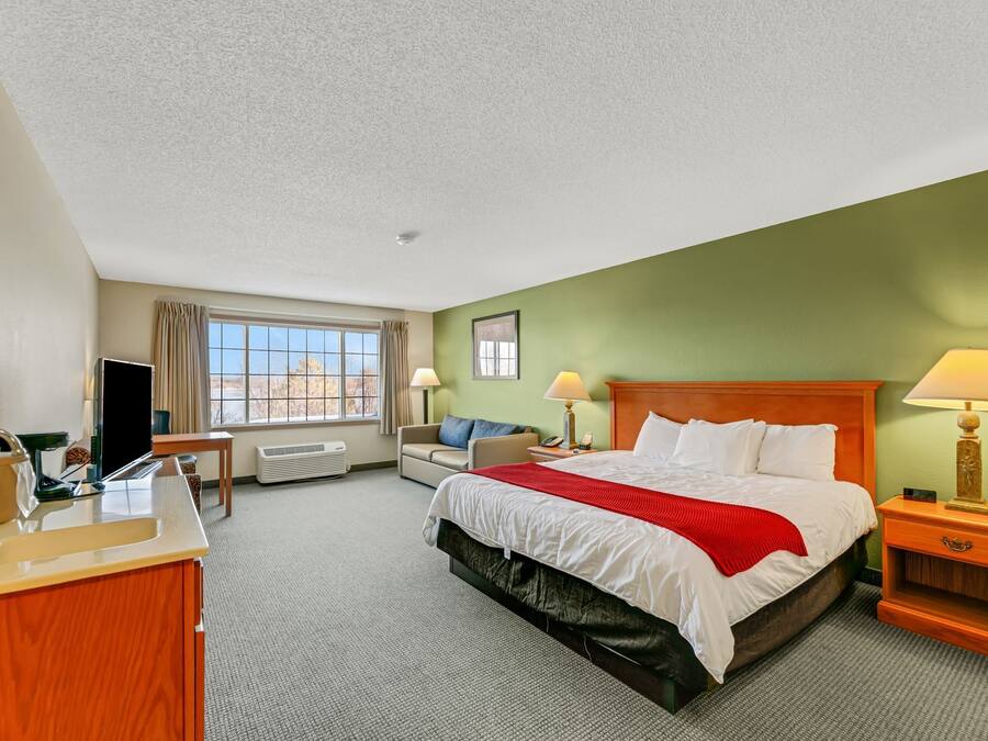 Une chambre d’hôtel comprenant un lit, un bureau avec un lavabo, une chaise, une fenêtre avec des rideaux et une lampe.